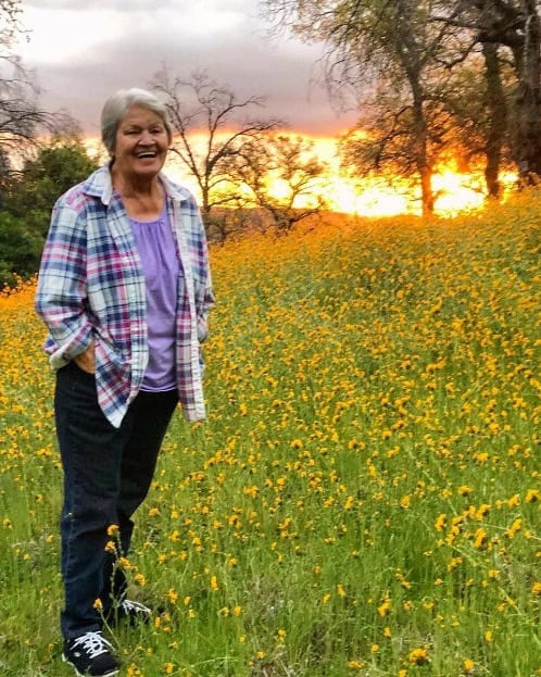 Woman smiling in a field of yellow flowers at sunset.