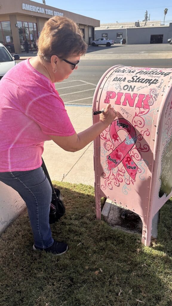 Woman placing a pink ribbon sticker on a breast cancer awareness mailbox.