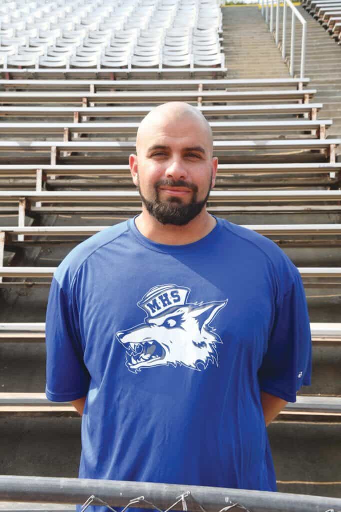 Man in blue Madera High School sports jersey at stadium.