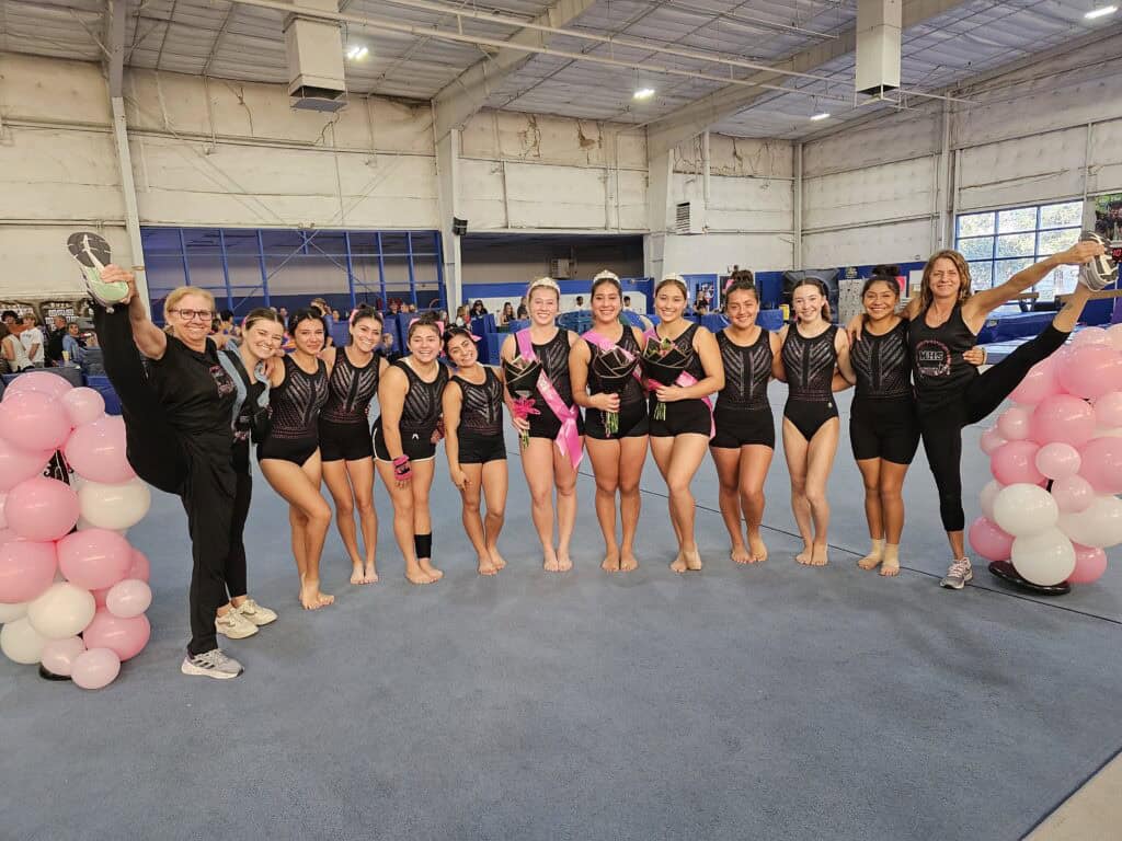 Madera gymnastics team celebrating with medals and balloons indoors.