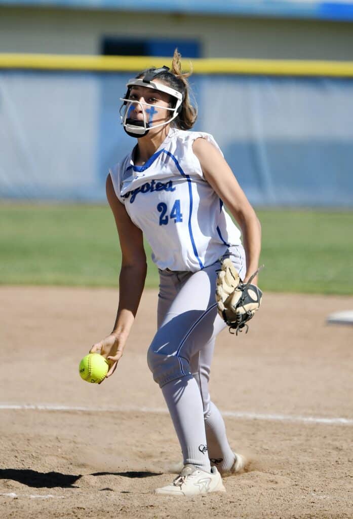 Softball player wearing protective gear, holding a yellow softball, ready to catch or throw.