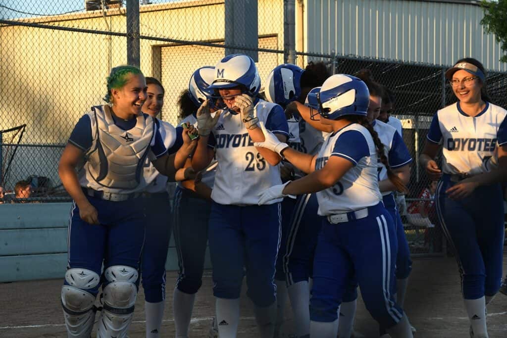 Softball players in blue and white uniforms celebrate after a game.