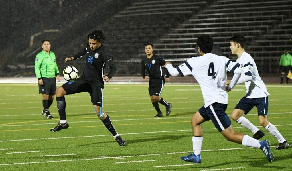 Players competing in a rainy soccer game on a wet field.
