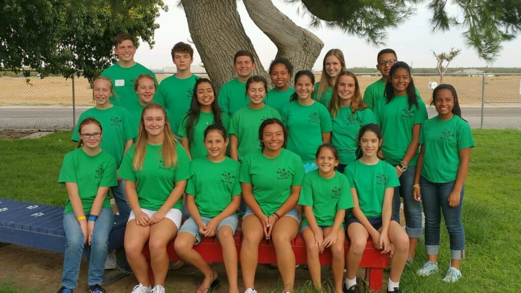 Group of diverse children and teenagers wearing matching green T-shirts outdoors.
