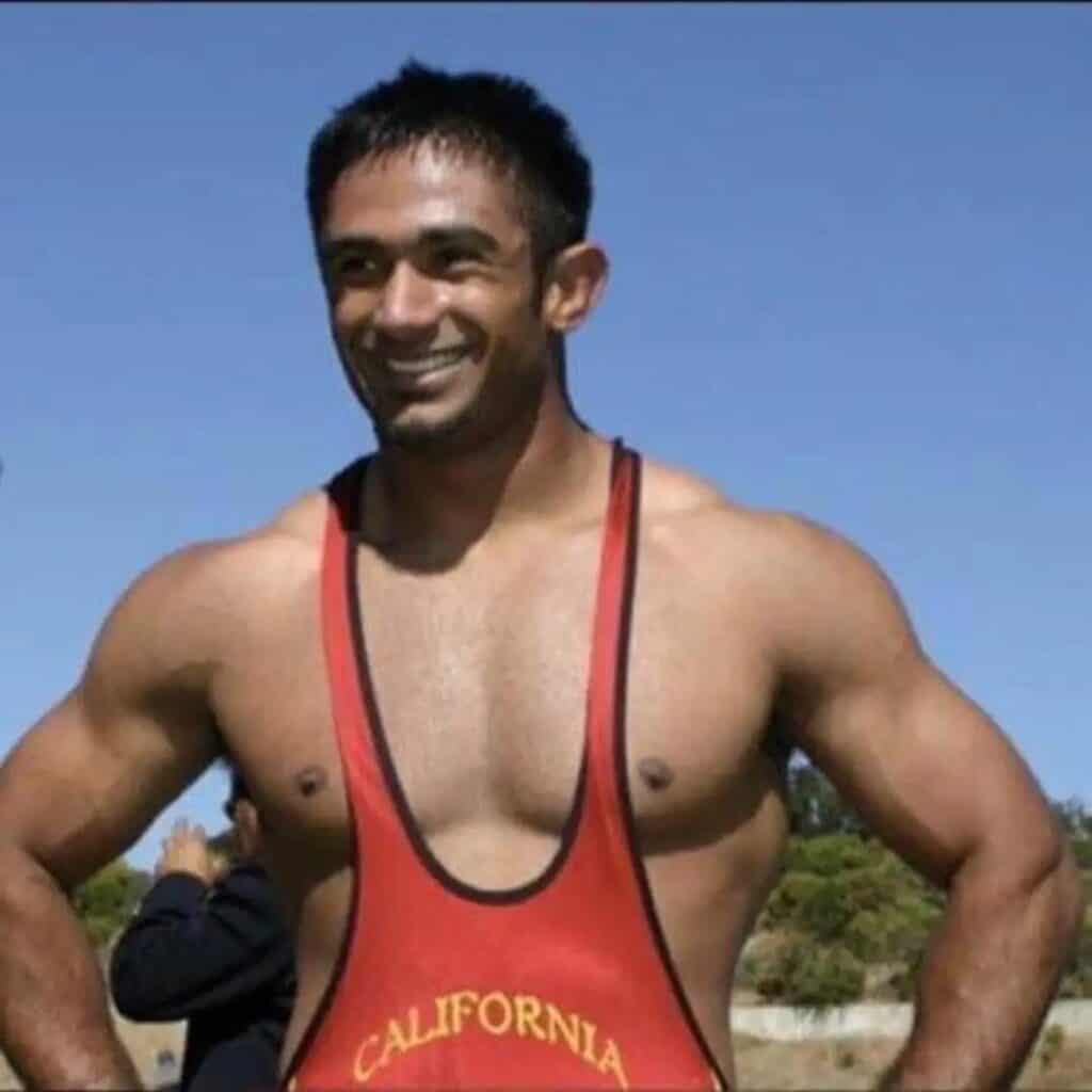 Male wrestler in red singlet outdoors with blue sky background.
