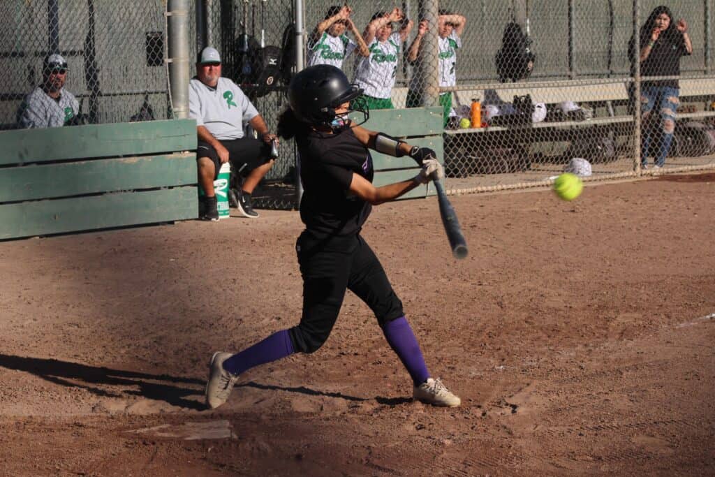 Young girl swinging softball bat during game at Madera softball field.