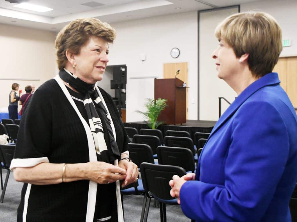 Two women conversing at a community event in a conference room.