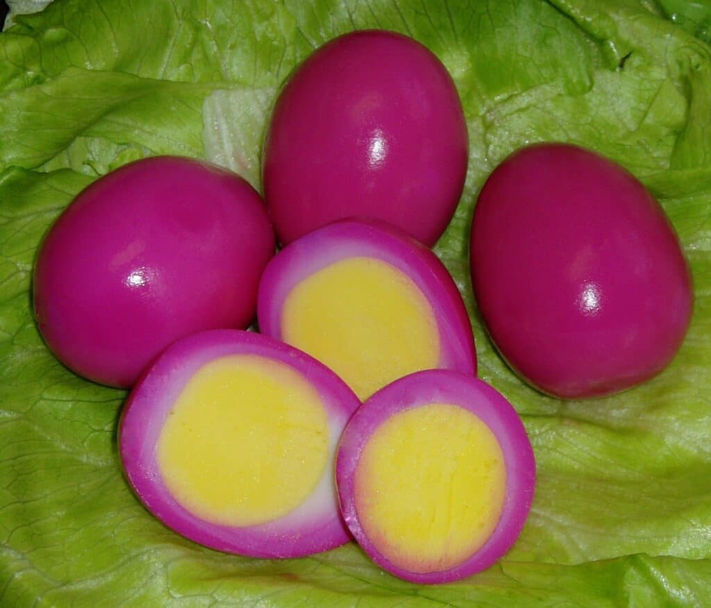 Radishes with vibrant pink skin and yellow interior on fresh lettuce leaves.