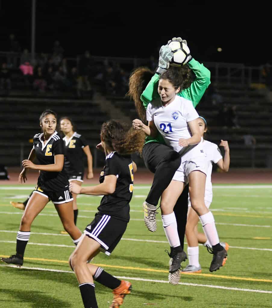 Female soccer goalkeeper catching ball during game at night.