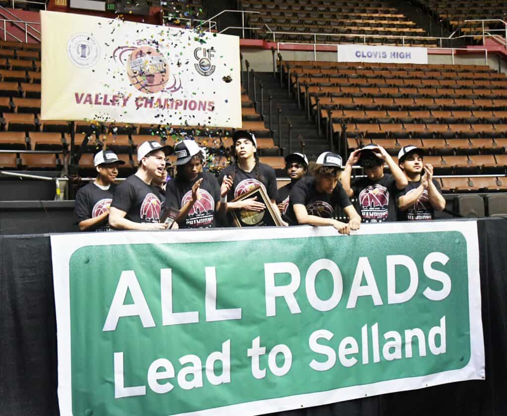 Youth basketball team holding a banner at a sports arena after winning a championship.