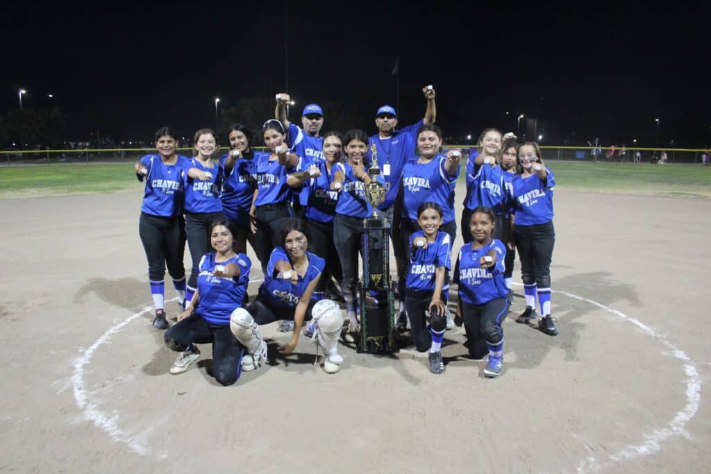 Madera softball team celebrating victory on the field at night.