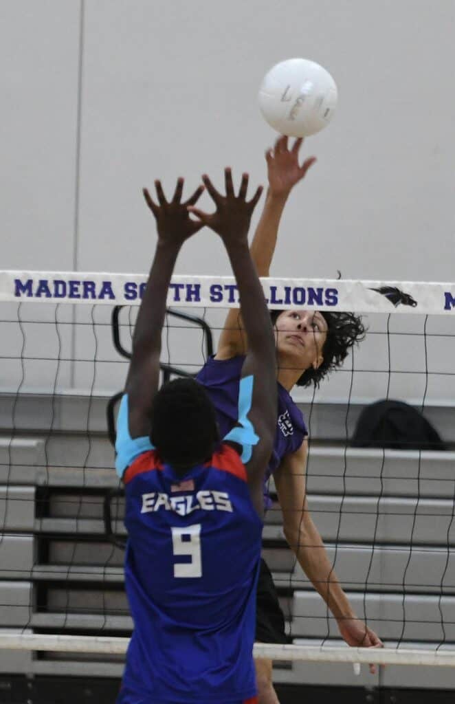 Female volleyball player spiking the ball over the net during match.
