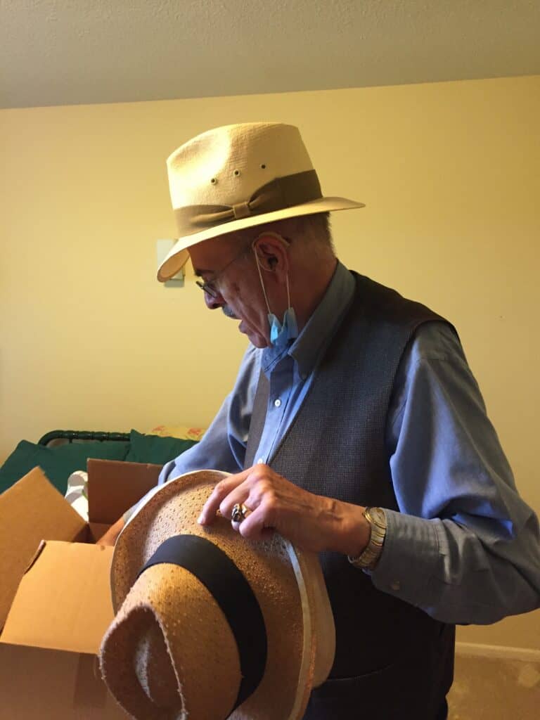 Man with hat inspecting a straw hat in an indoor setting.
