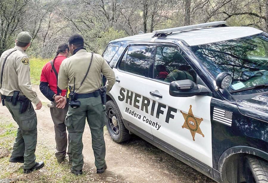 Madera County sheriff officers with patrol vehicle in wooded area.