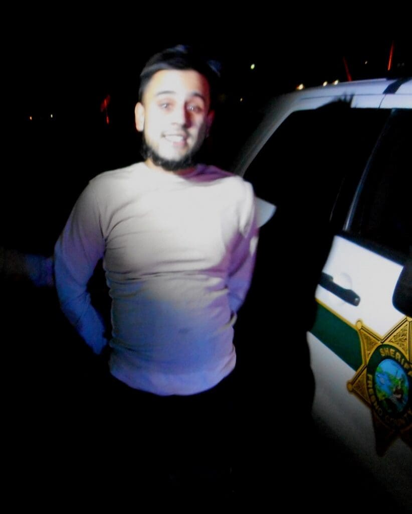 Young man with a beard standing next to a police vehicle at night.
