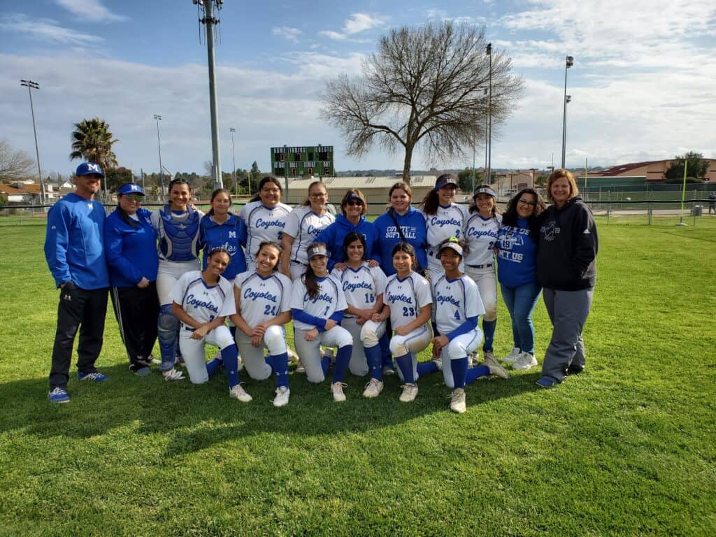 Madera Coyotes softball team posing outdoors on a sunny day.
