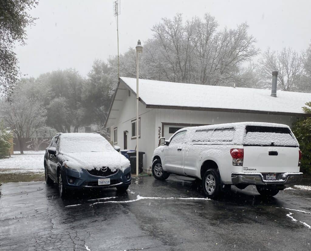 Snow-covered cars parked outside a building in Madera during winter.