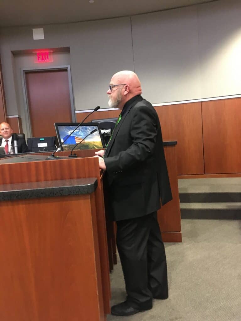 Bald man speaking at a podium during a formal event.