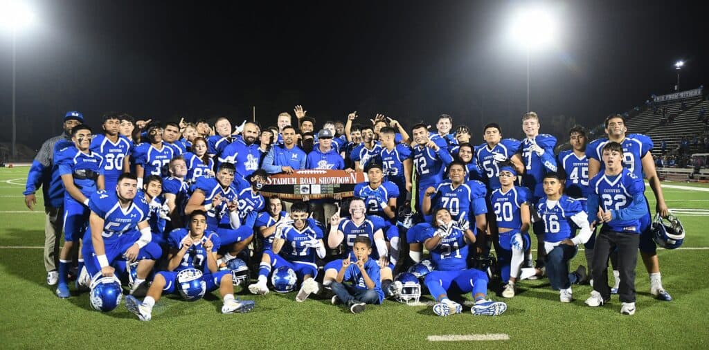Youth football team in blue uniforms celebrating victory on the field.