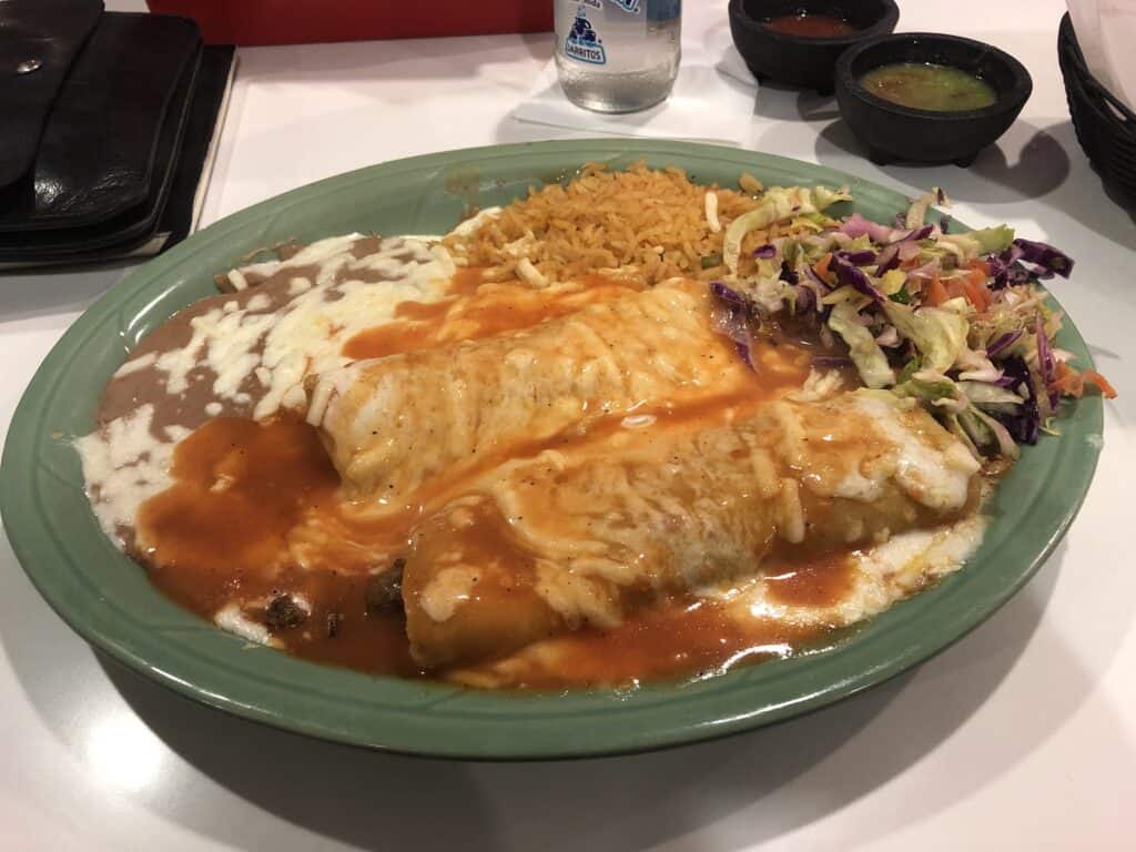 Delicious mole enchiladas served with rice and fresh salad on a green plate.