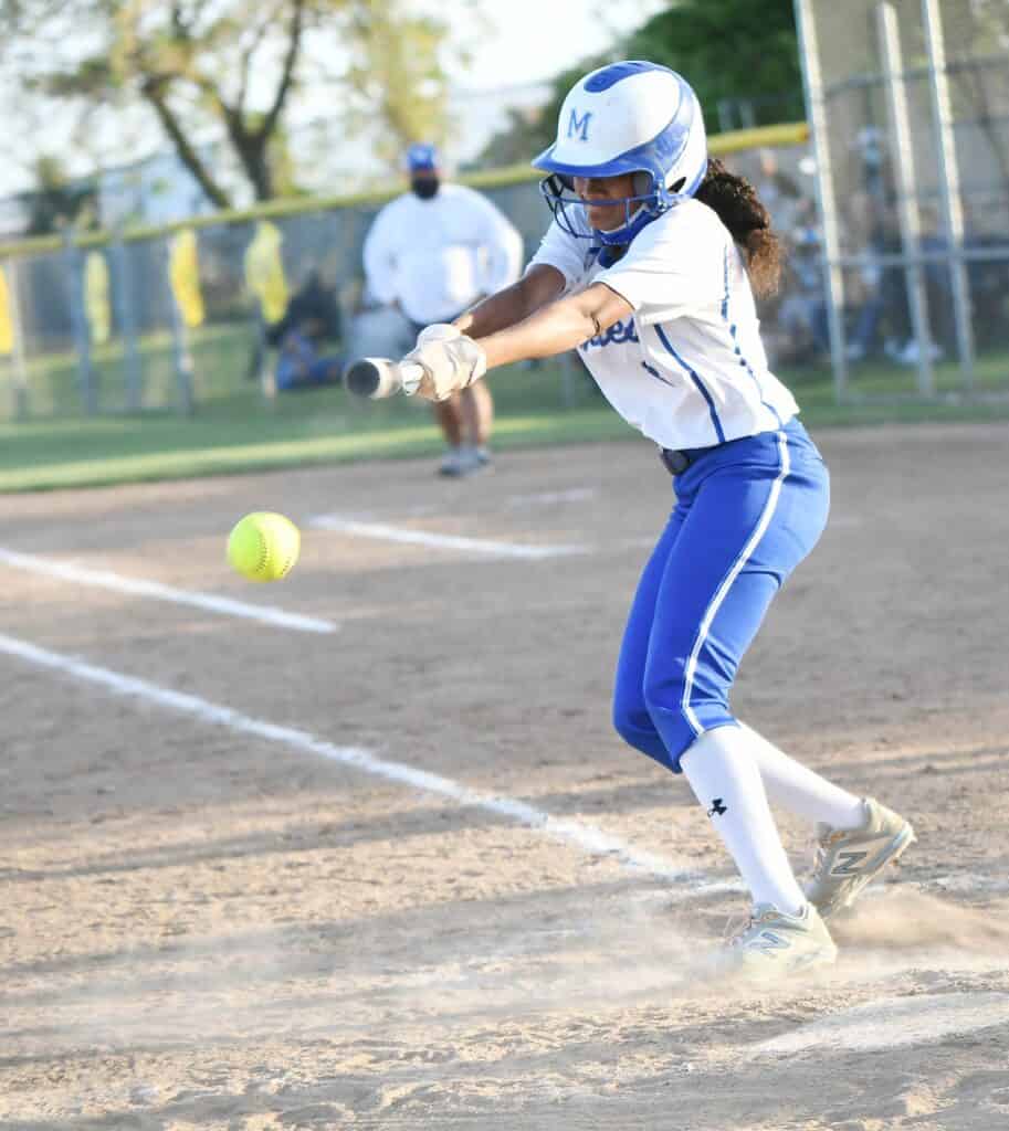 Young female softball player swinging at a pitch during a game.