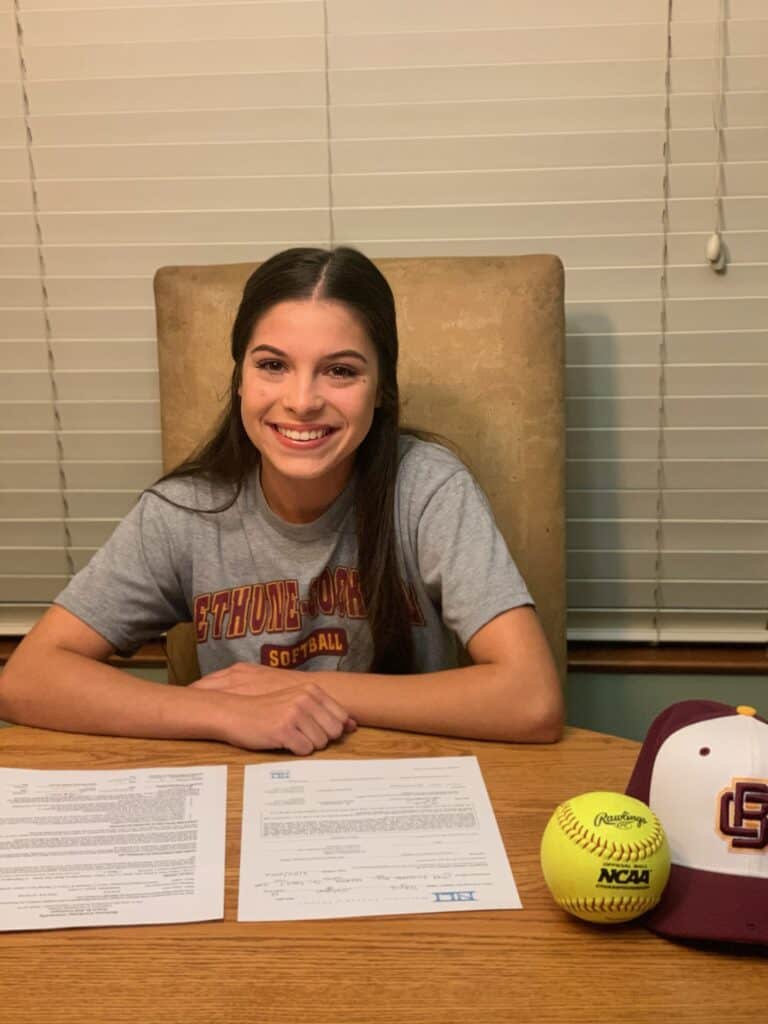 Softball player signing her college commitment at a table.