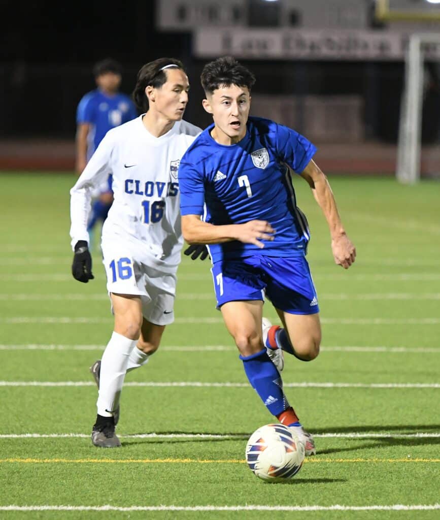 Young soccer player in blue jersey dribbling ball during match.