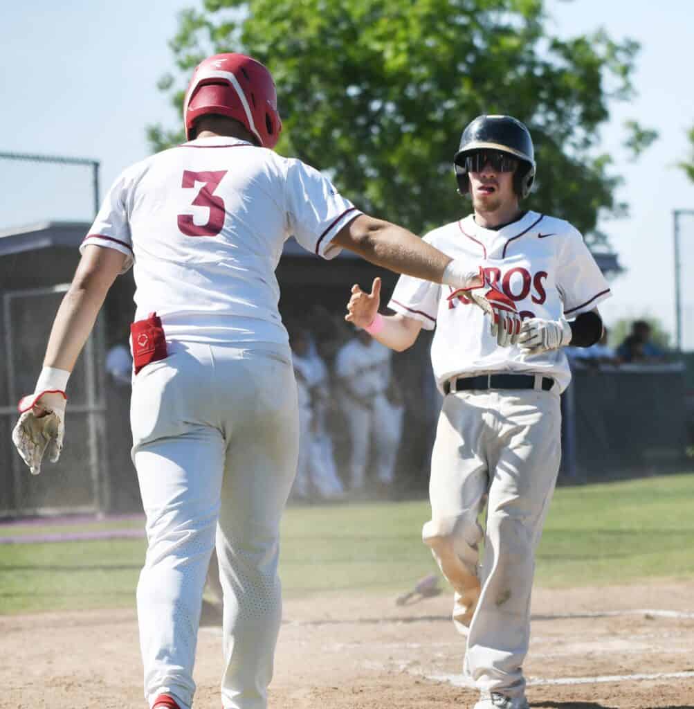Two young baseball players celebrating on the field after scoring.