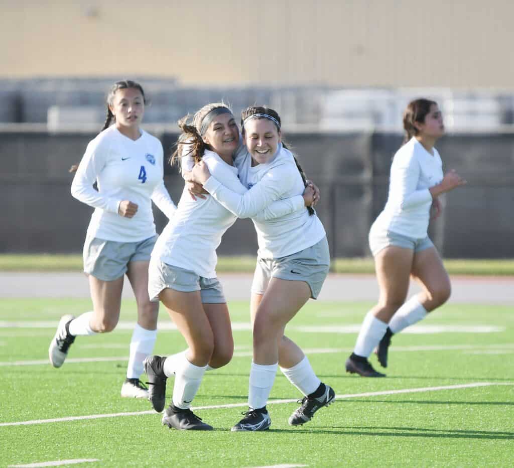 Girls' soccer team celebrating victory on the field.
