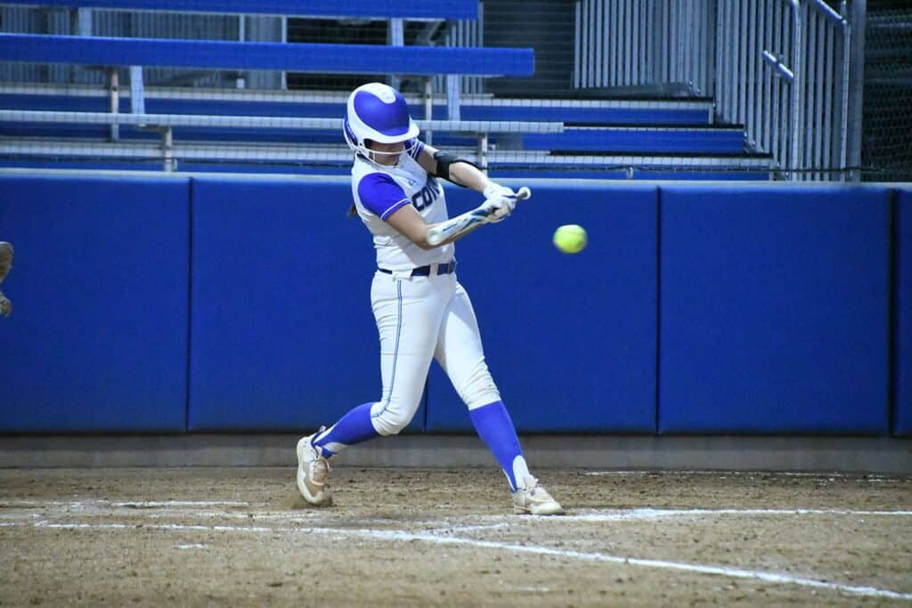 Female baseball player swinging at a pitch during a game.