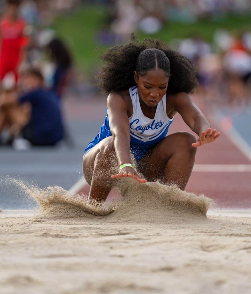 Female athlete landing in sand pit during long jump event.