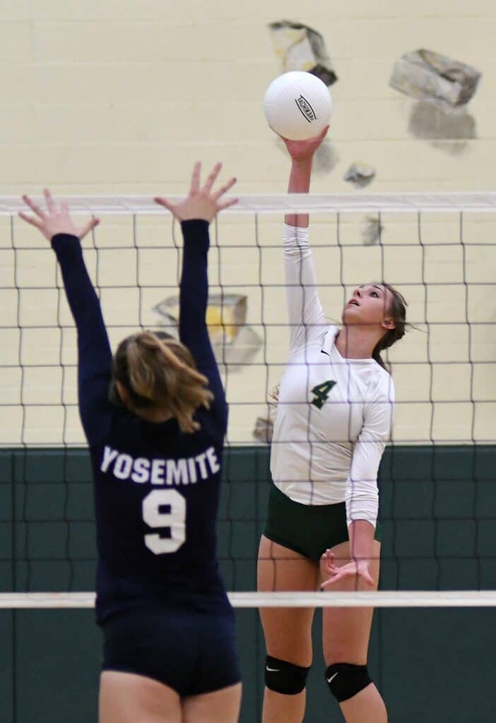 Female volleyball player spiking ball over net during game.