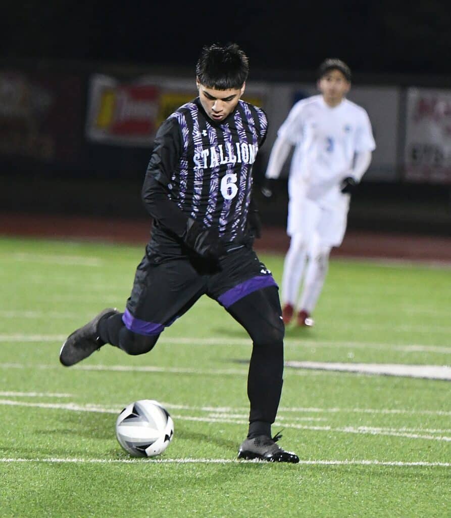 Soccer player in black and purple uniform kicking the ball during a match.