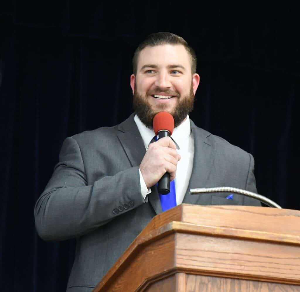 Man speaking at a public event with a microphone and podium.
