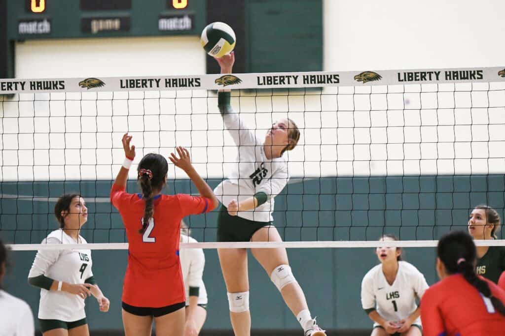 Volleyball player spikes the ball over the net during a match.