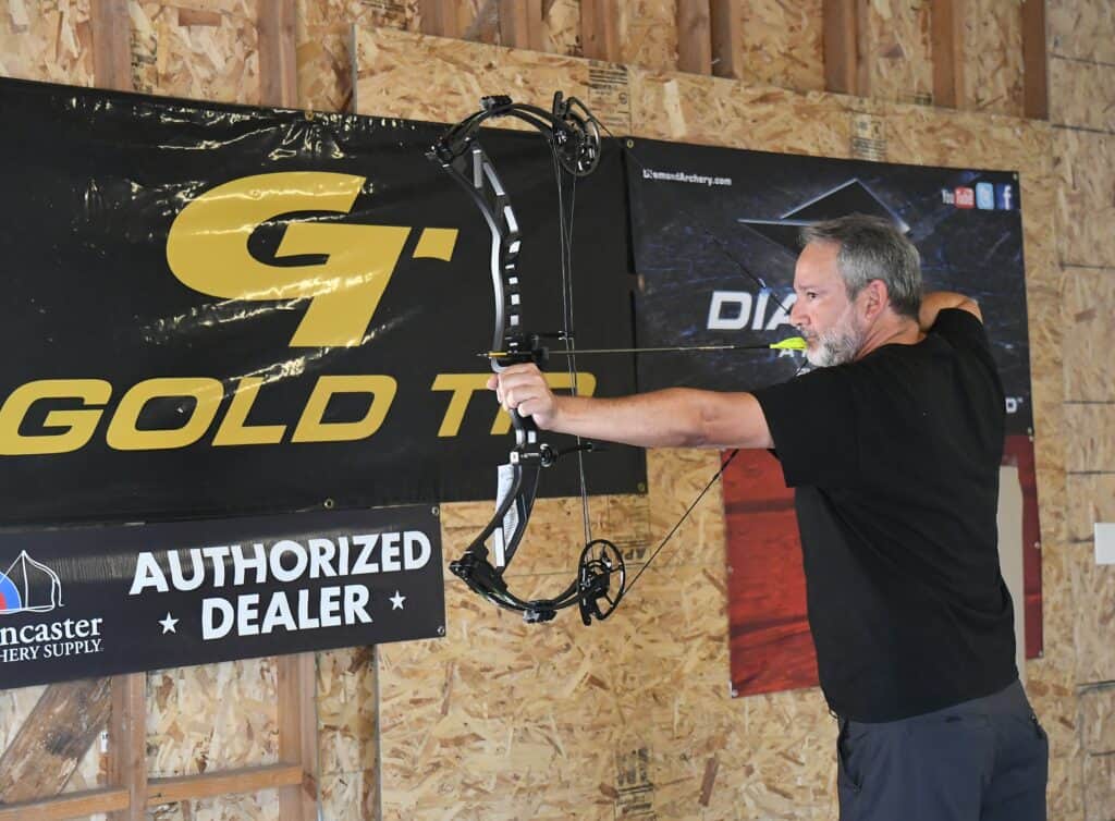 Archery enthusiast aiming at target with bow and arrow indoors.
