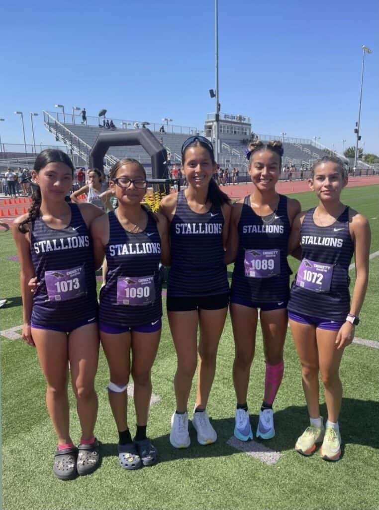 Young female athletes in matching uniforms pose on the track.