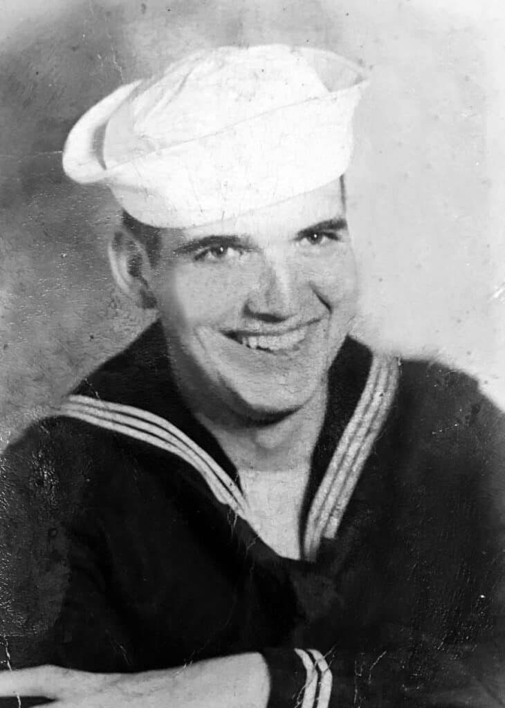 Sailor in uniform with a white hat, smiling for the camera.