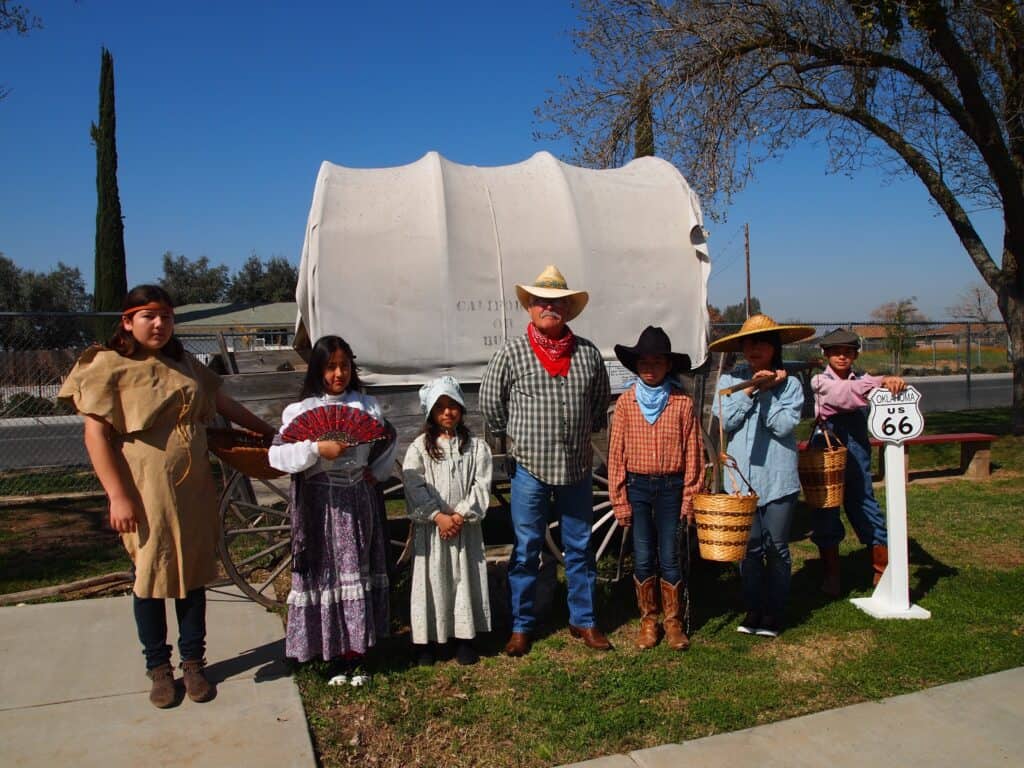 Group of people dressed in historical costumes with wagon display in Madera park.