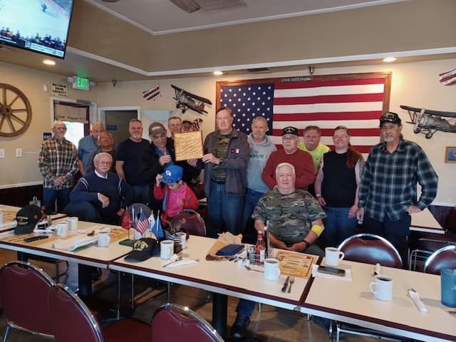 Veterans group photo at Madera restaurant with American flags and military memorabilia.