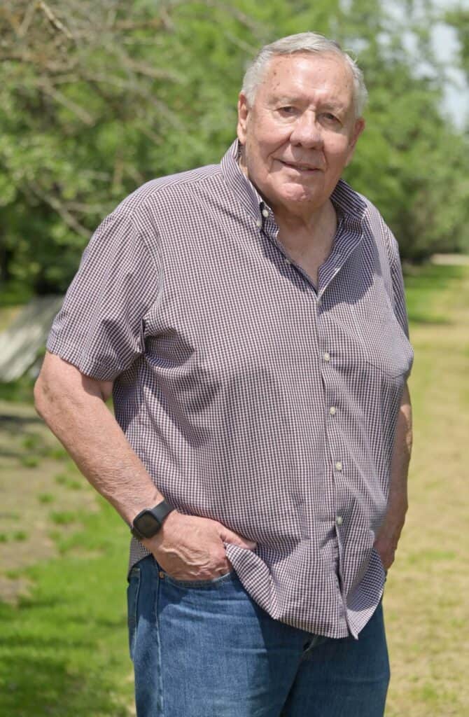 Senior man standing outdoors in a park, smiling at the camera.