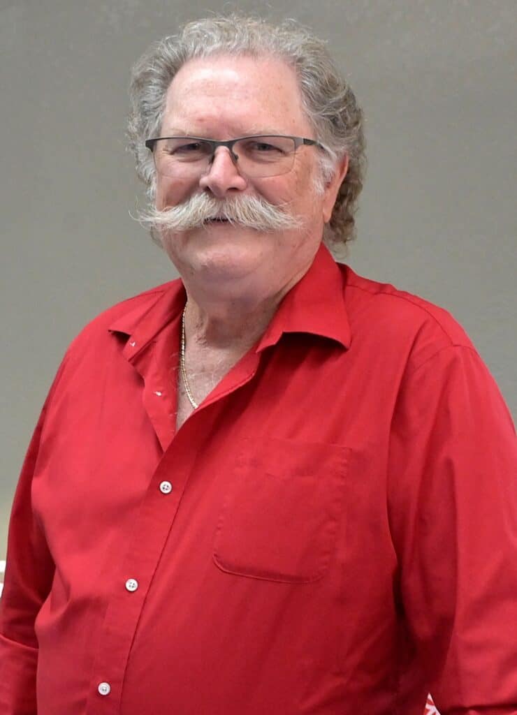 Man with gray hair and mustache wearing glasses and a red shirt.