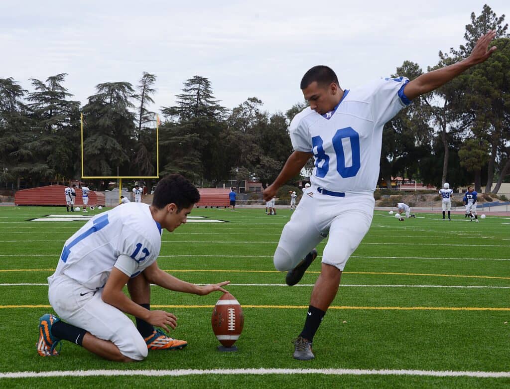 Football players practicing on the field with a focus on kicking and teamwork.