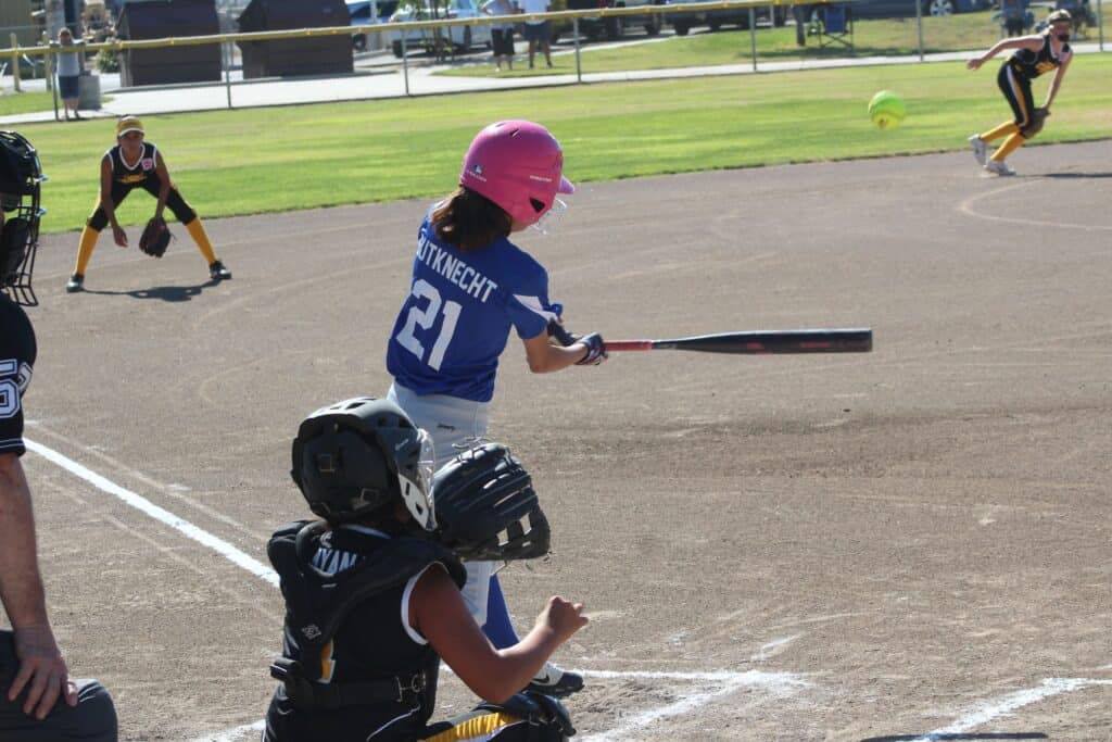Young girl in blue uniform swinging a bat during a youth baseball game.