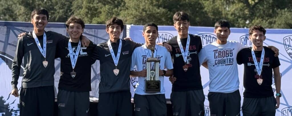 Photo of The Matilda Torres Toros boys cross country team holds the trophy on stage after wining its second straight County/Metro Athletic Conference championship. Benjamin Fernandez, holding trophy, won the individual title, as well.