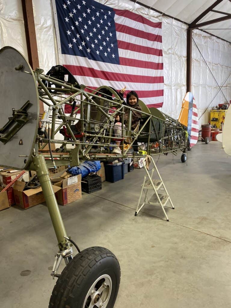 Photo - Piper Hoffrage sits in the deconstructed body of a PT-17 Stearman that her father, Mike Hoffrage is working on rebuilding. Hoffrage is now working on creating the Central Cal. Aviation Museum in an old hanger at the Madera Airport.