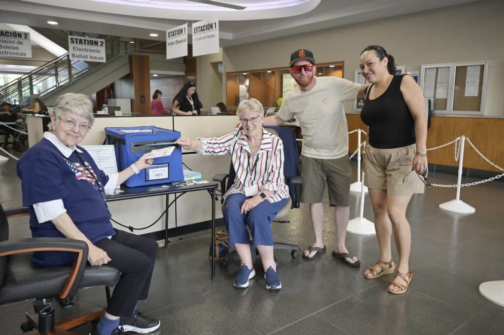 Photo - Election workers Judy Sears, left, and Carol Kennedy, collect ballots from Matt Patrick and Kristi-Ann Anderson at the Madera County Government Center on Tuesday.