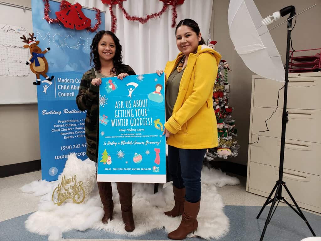 Two women holding a sign about winter goods at child abuse prevention event.