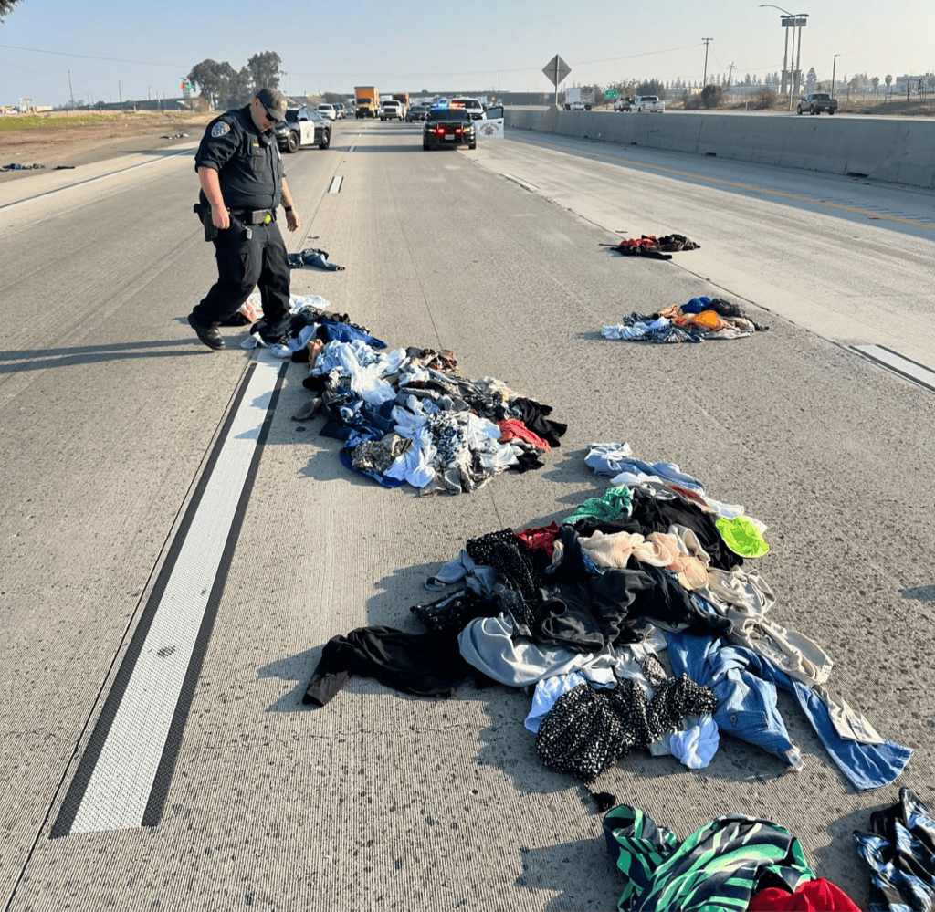 Emergency responder inspecting scattered clothes on highway.