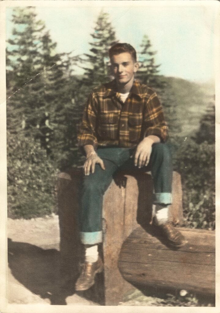 Older boy sitting outdoors on a wooden bench, smiling.